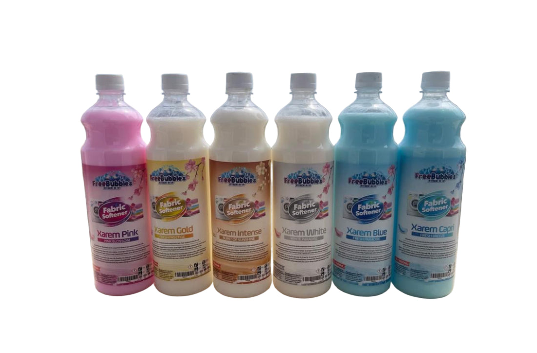 Six bottles of fabric softener in different colors on a wooden surface with a scenic background.